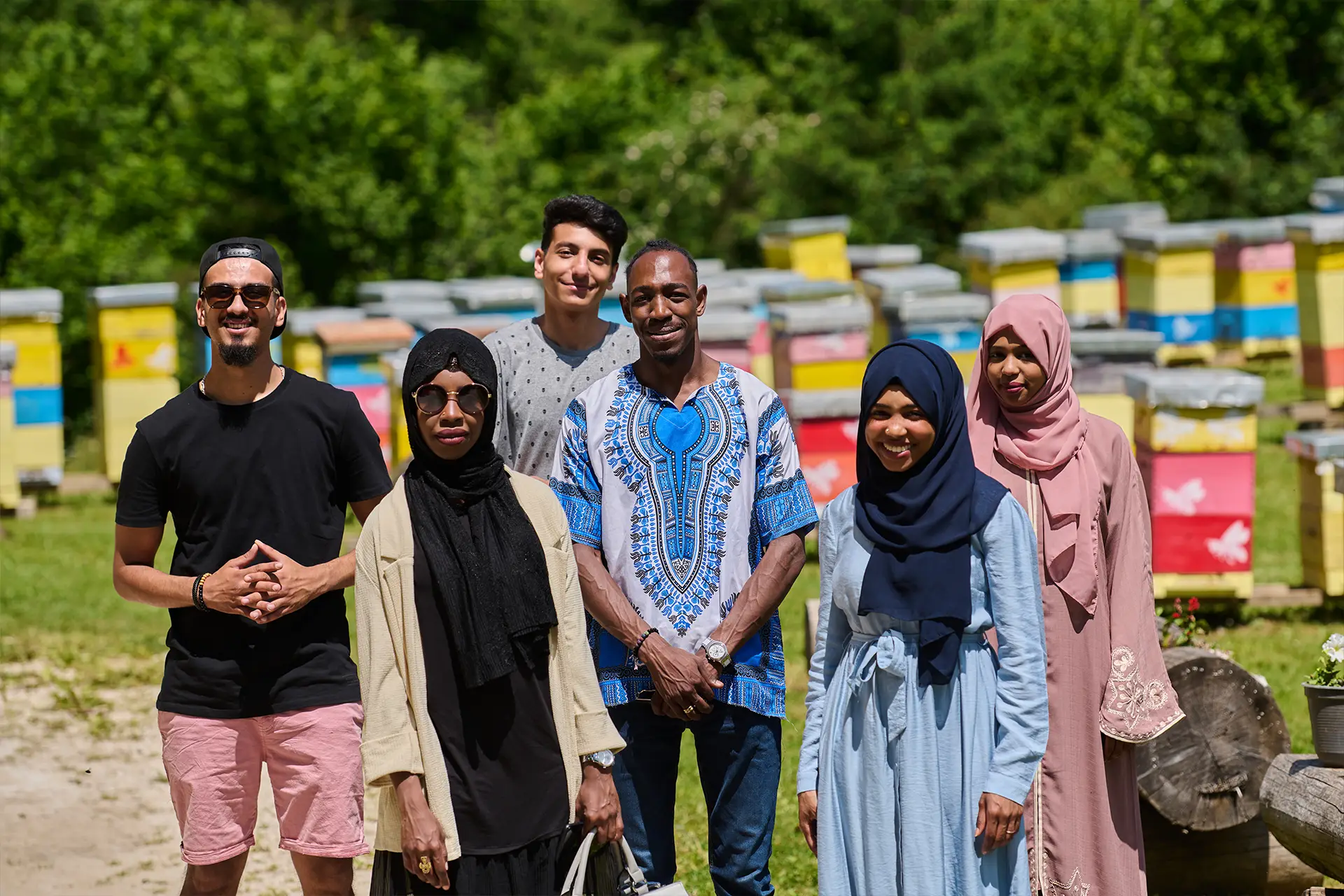 Six volunteers from diverse backgrounds smiling by beehive boxes in Leeds, helping a local charity on a sunny day.