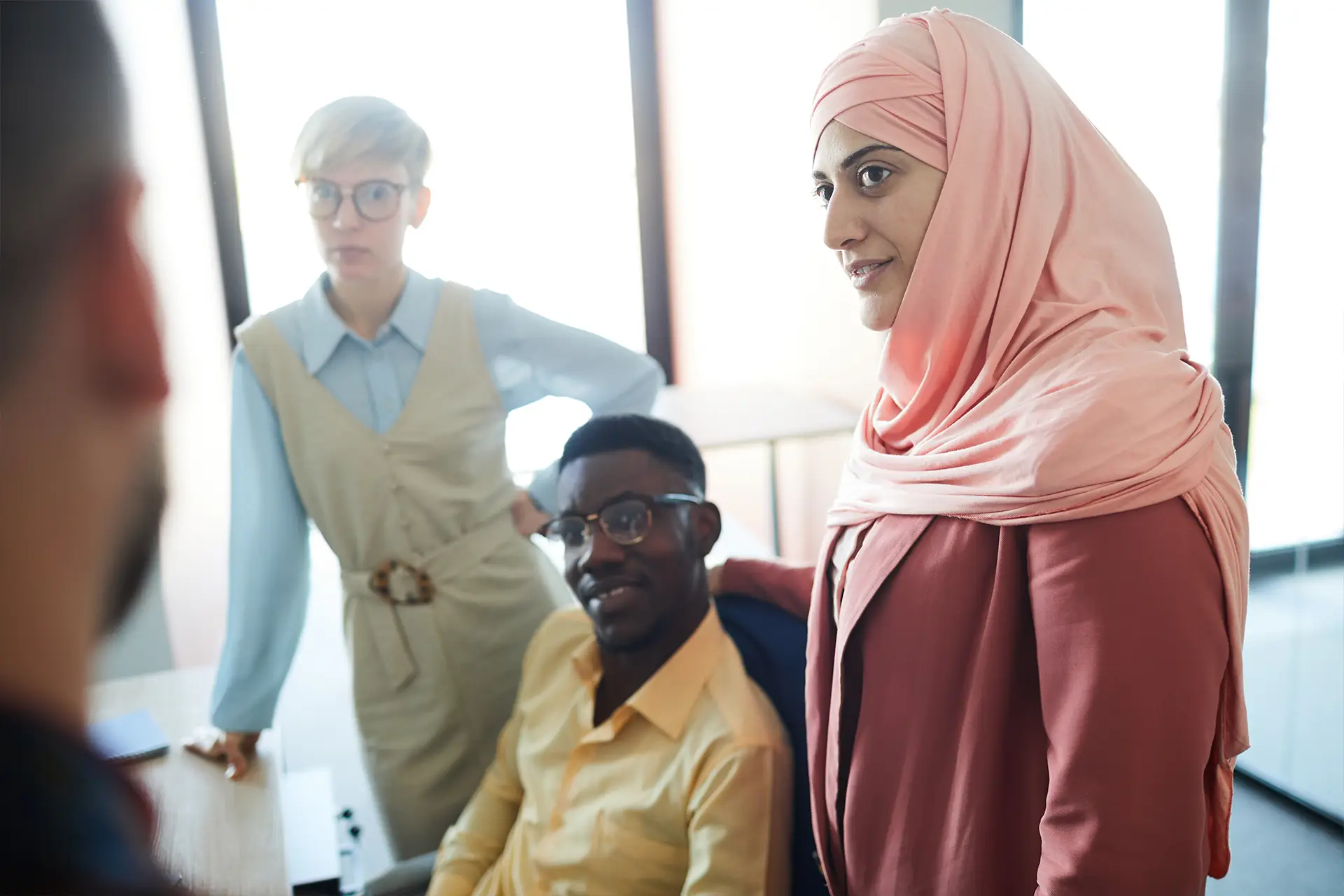 Three people talk with a fourth person in a bright office, Leeds; diverse volunteers at a Doing Good Leeds meeting.