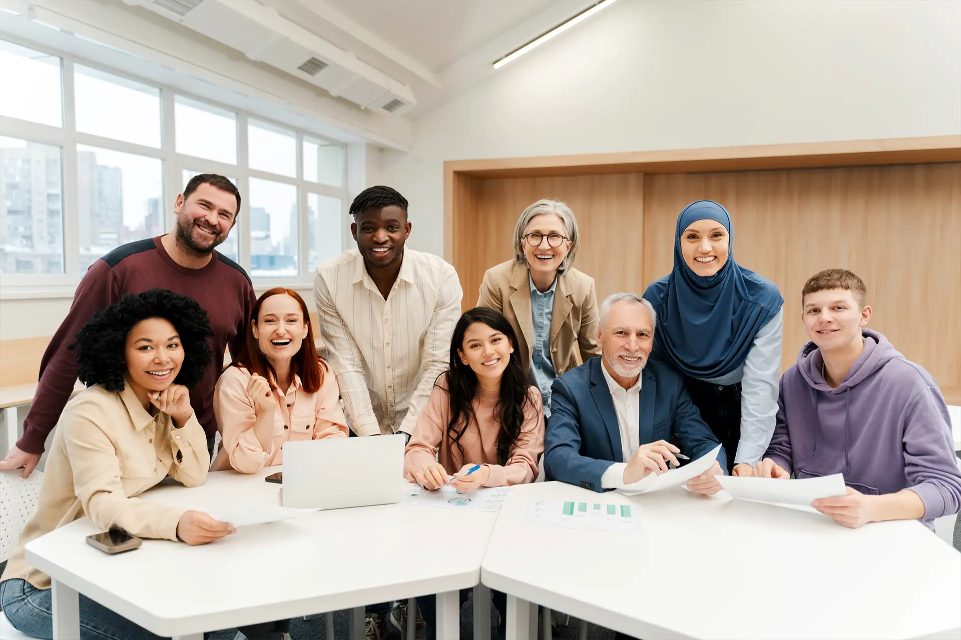 Nine people smiling together around a table with papers and a laptop, collaborating in Leeds for Doing Good Leeds volunteering project.