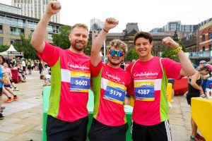 Three men in pink Candlelighters shirts celebrate finishing the Leeds 10K, supporting charity in Leeds.