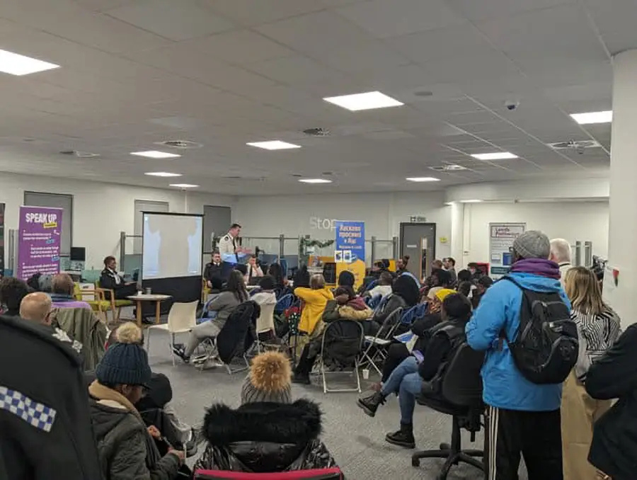 Community members watch a presentation in a busy Leeds conference room with banners for local volunteering projects, Doing Good Leeds.