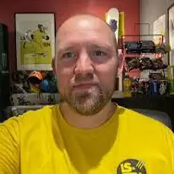 Man with shaven head and short beard in yellow T-shirt sits in welcoming Leeds office, Young Lives Leeds volunteering space.