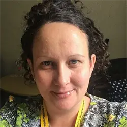 Woman with curly brown hair smiles, yellow lanyard visible, supporting youth advocacy in Leeds for Doing Good Leeds.