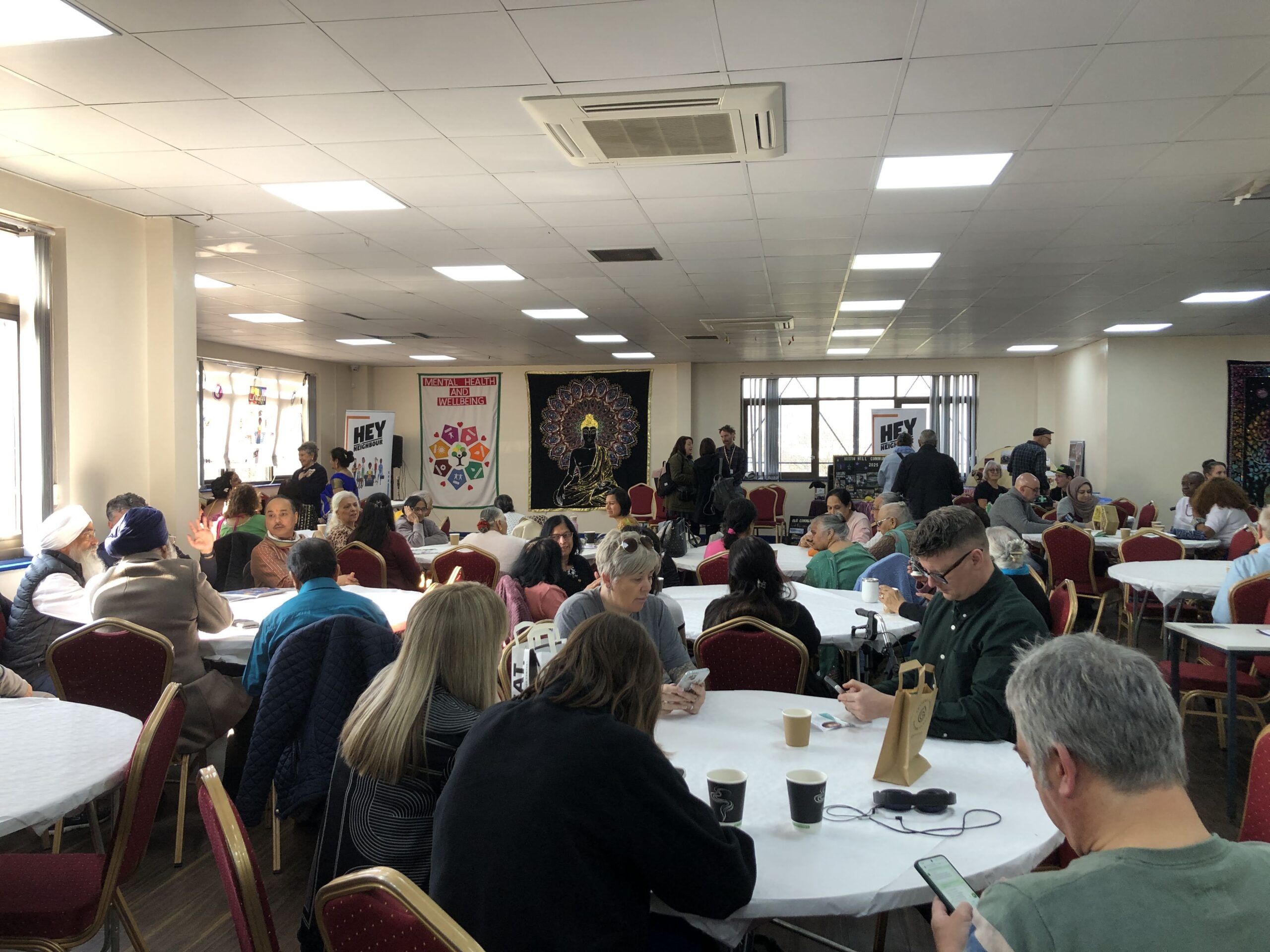 People at round tables chatting and eating in a bright Leeds venue, with banners, for a Doing Good Leeds community event.