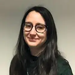 Woman with long dark hair and glasses smiles at camera, Leeds, highlighting youth advocacy at Young Lives Leeds.