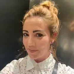 A woman from Young Lives Leeds smiles at the camera, wearing a white blouse; portrait for Doing Good Leeds charity section.
