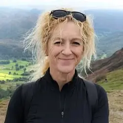 Woman with curly blonde hair smiles outdoors on green hills, supporting youth advocacy in Leeds with Leeds Advocates.